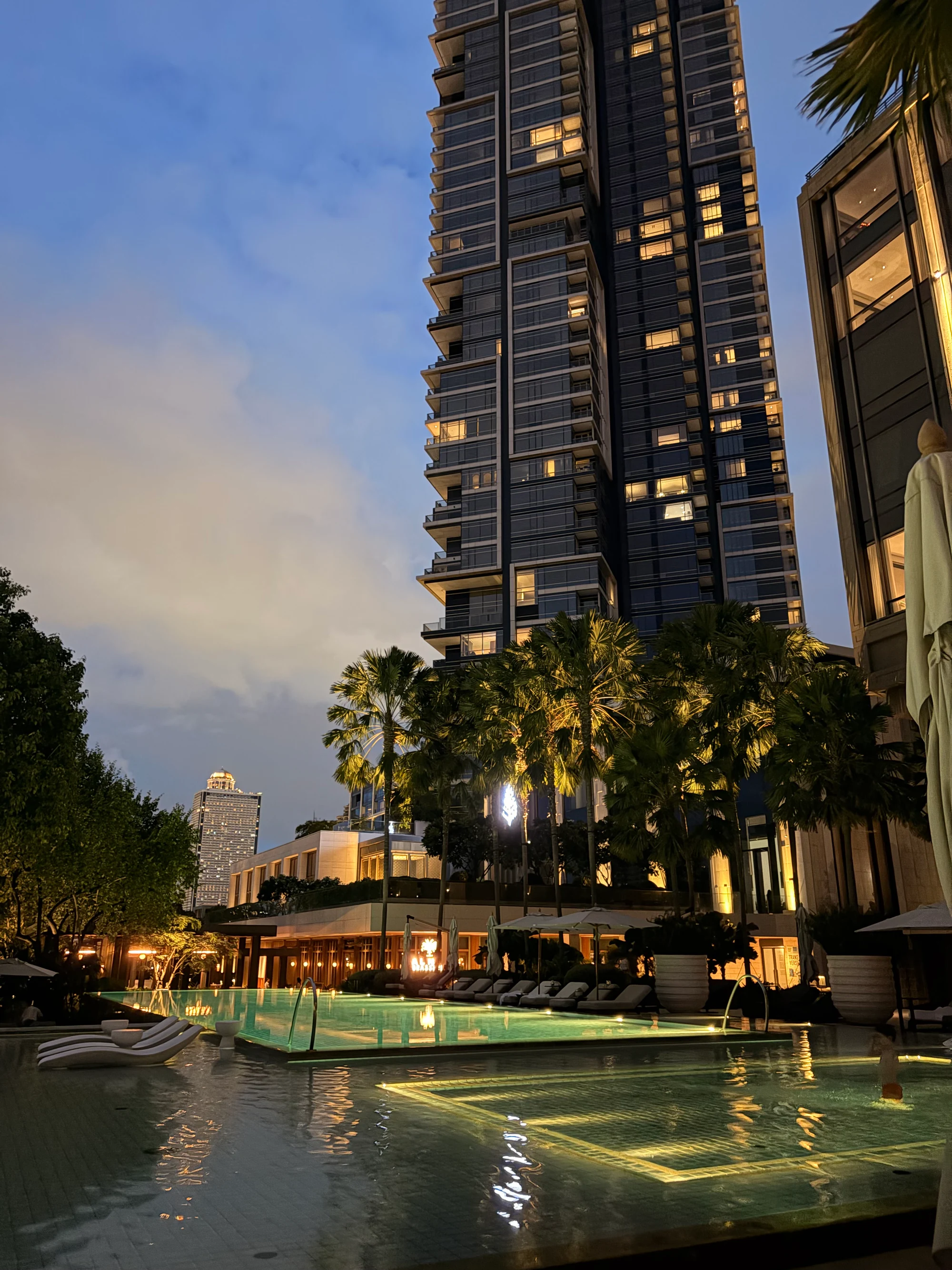 Terrasse de la piscine du Four Seasons Hotel Bangkok à la tombée du jour, avec la tour résidentielle voisine en arrière-plan