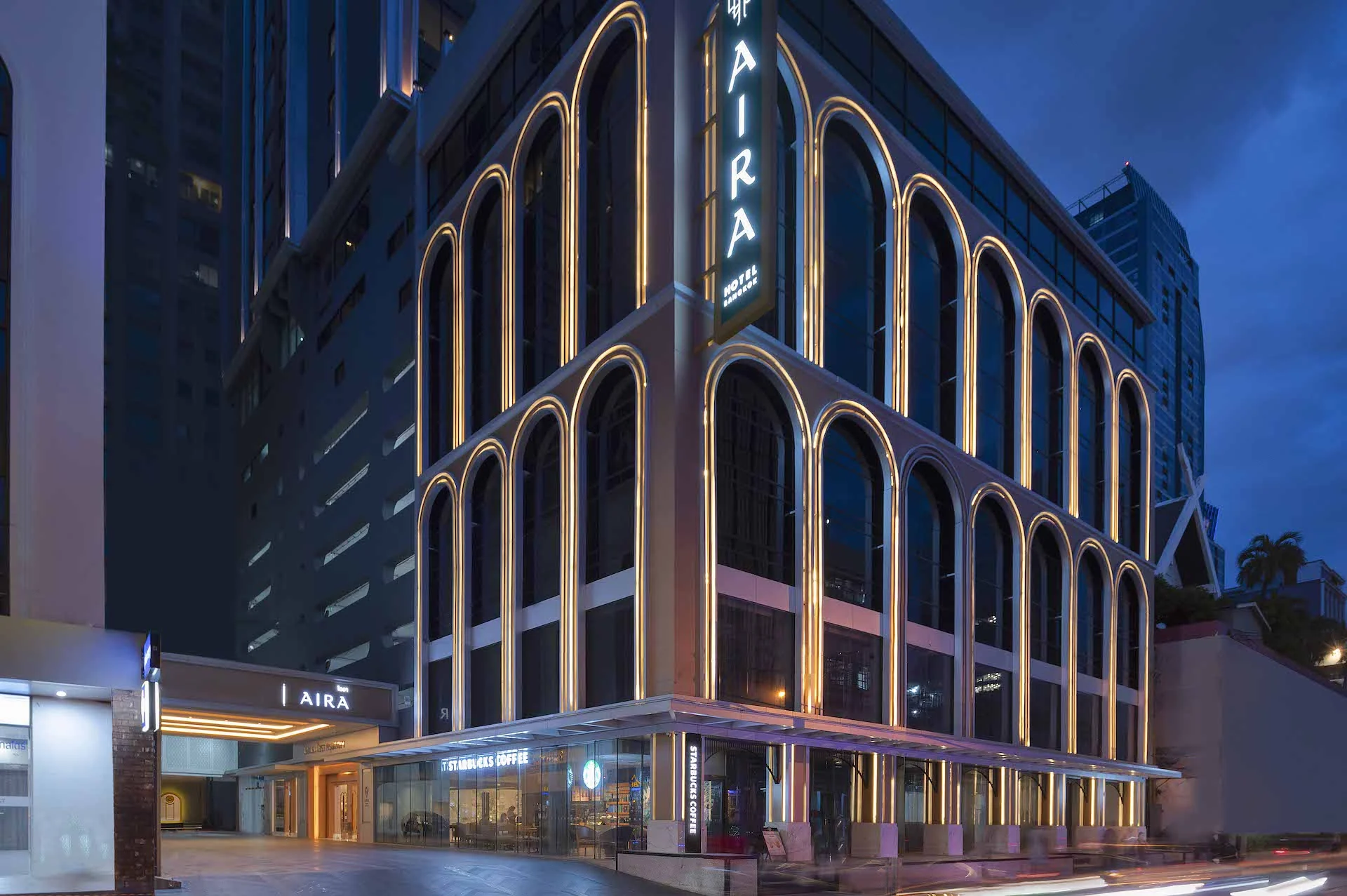 Aira Hotel Bangkok’s illuminated arched facade, AIRA sign and street-level entrance at night