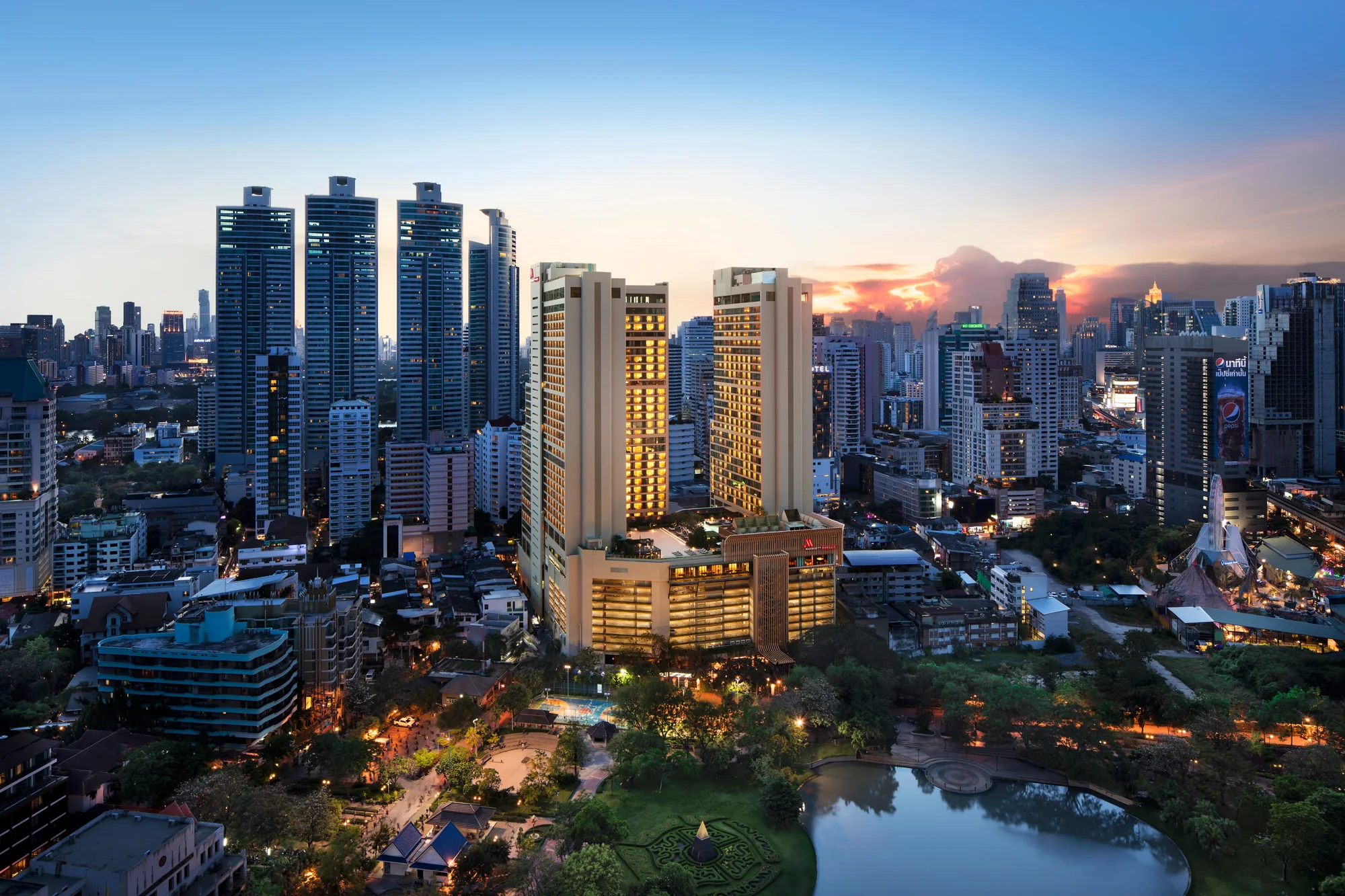 Les deux tours du Bangkok Marriott Marquis Queen’s Park et l’enseigne Marriott illuminée au-dessus du parc Benjasiri à la tombée du jour