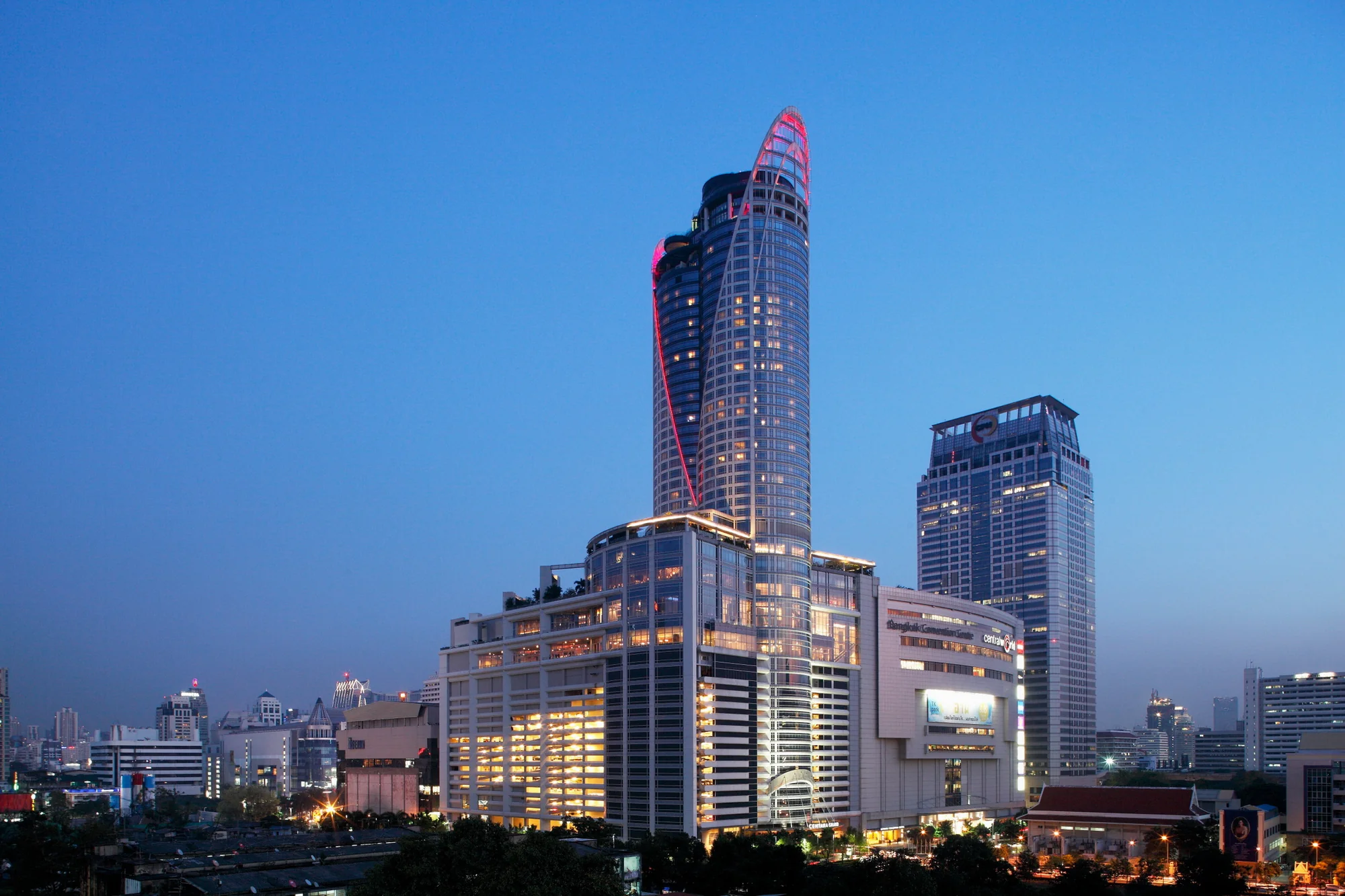 Der geschwungene Hotelturm über CentralWorld und dem Bangkok Convention Centre zur blauen Stunde.