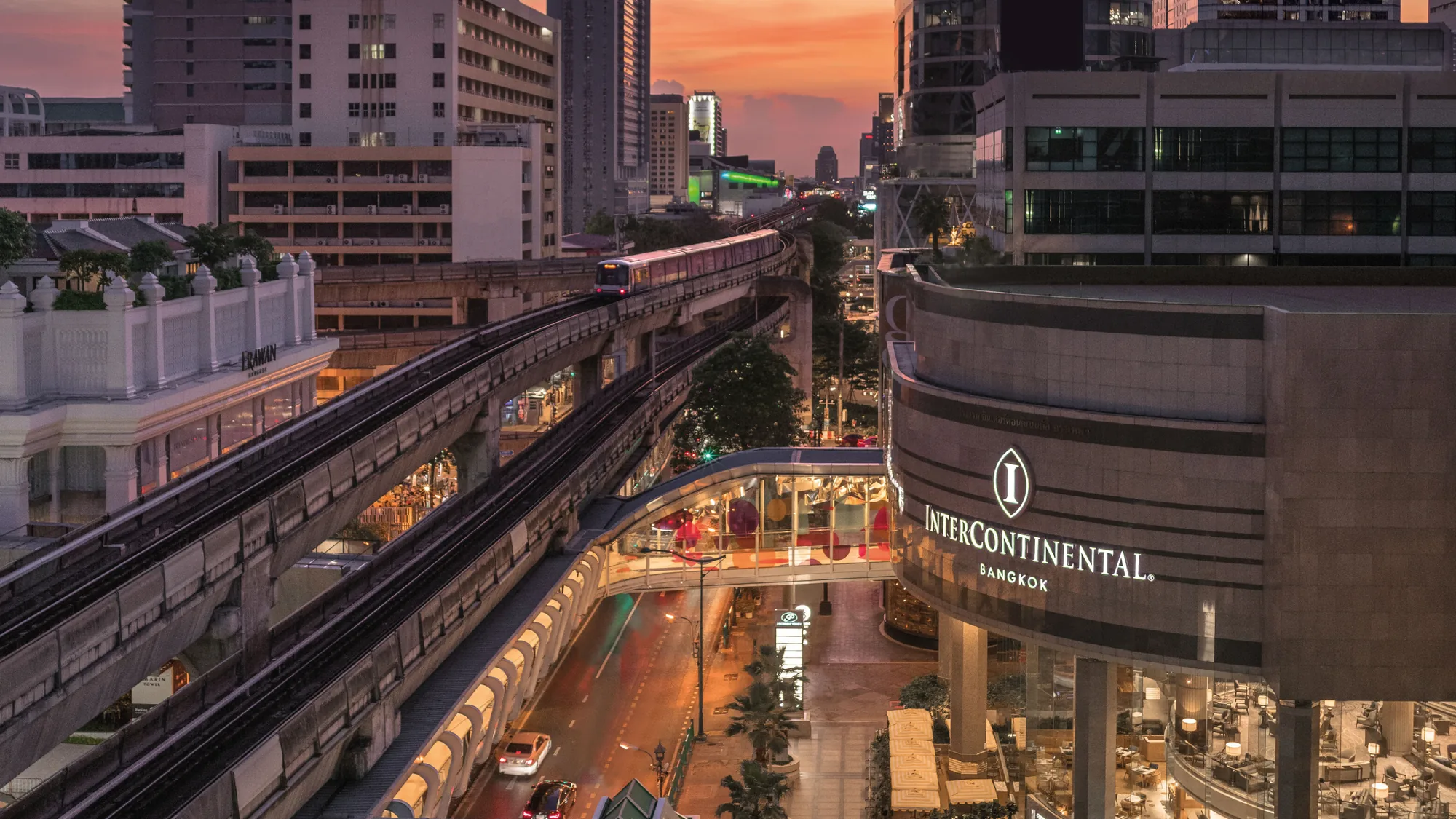 Fassade des InterContinental Bangkok mit beleuchtetem Hotelnamen an der Phloen Chit Road und dem Fußgängersteg in der Dämmerung