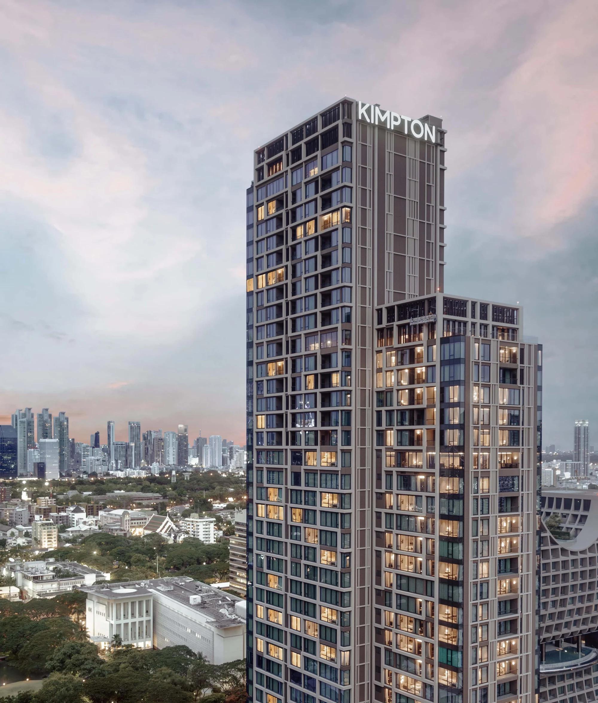 Der gestufte Turm des Kimpton Maa-Lai Bangkok mit großem KIMPTON-Dachschild über dem grünen Lang Suan bei Sonnenuntergang