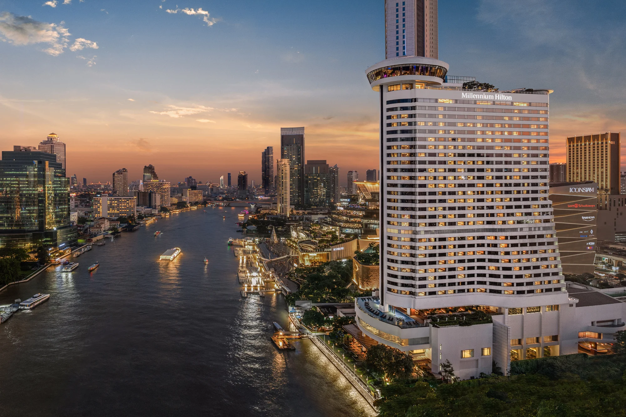 Millennium Hilton Bangkok mit beleuchtetem Hotelnamen am Chao Phraya in der Dämmerung