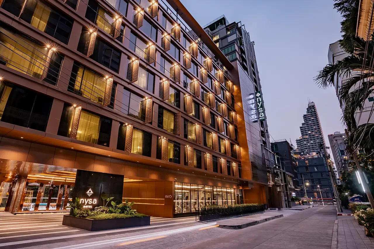 暮色中亮燈的 Nysa Hotel Bangkok 外牆、臨街入口與飯店招牌