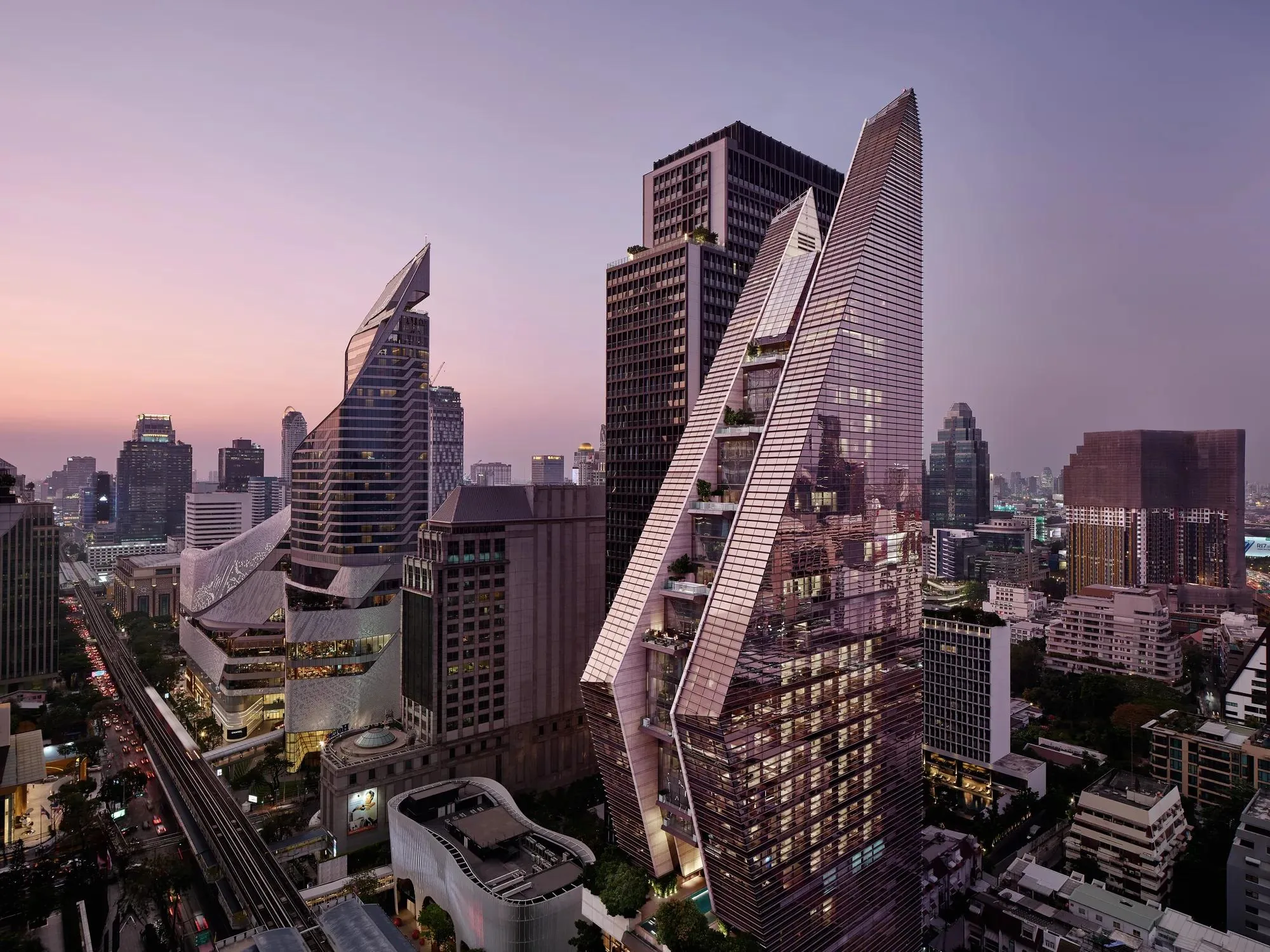 Rosewood Bangkok mit seiner markanten, schrägen Glasfassade über Phloen Chit in der Abenddämmerung