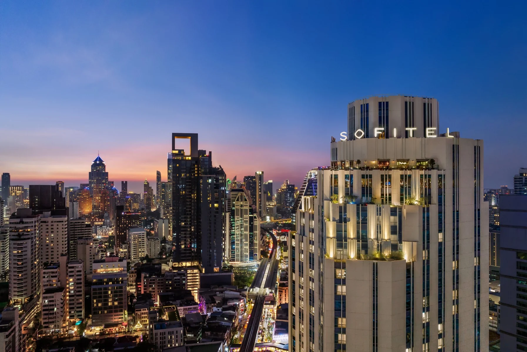 Sofitel Bangkok Sukhumvit’s illuminated hotel tower and large Sofitel sign above Sukhumvit Road at twilight