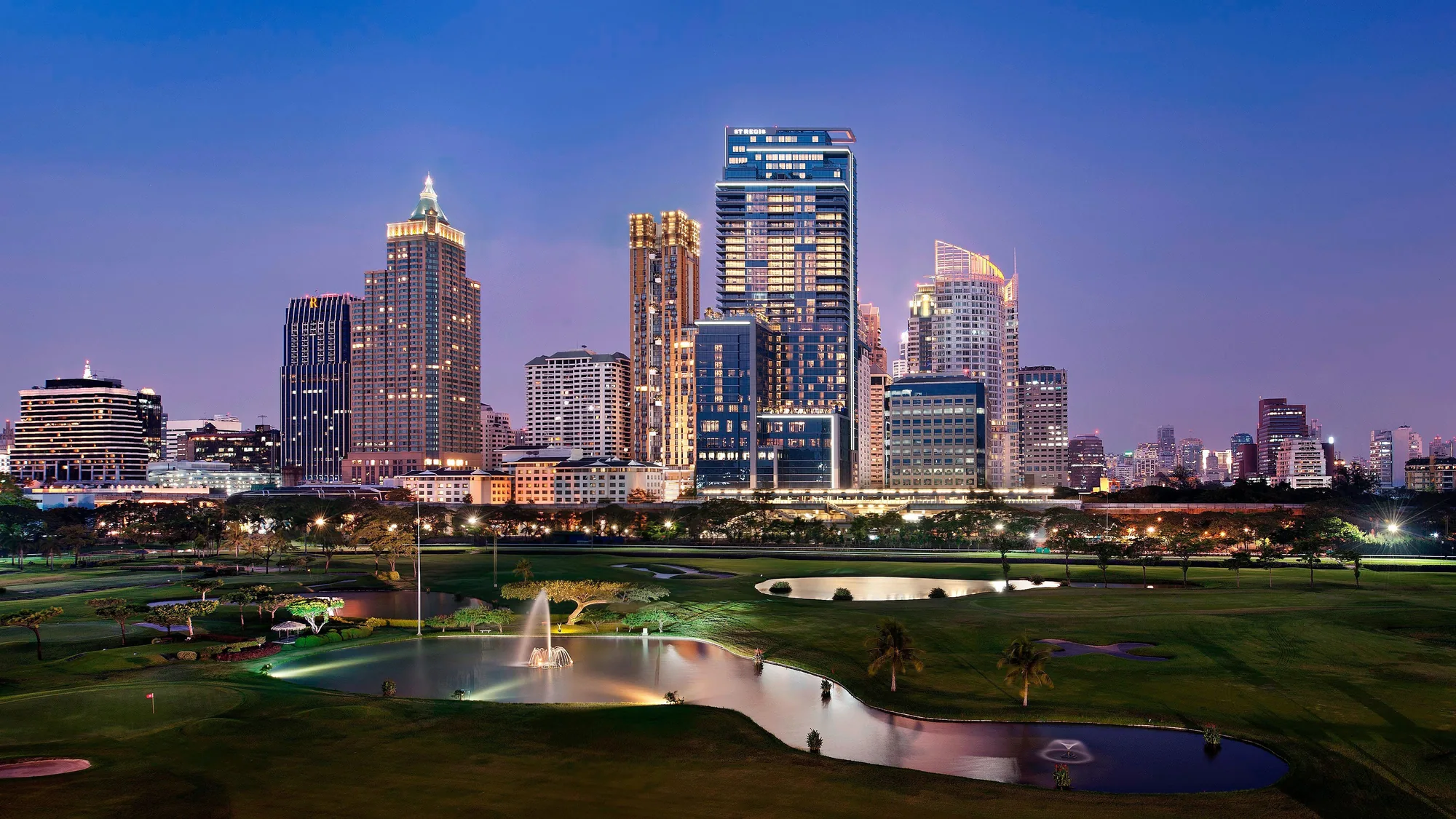 La tour du The St. Regis Bangkok et son nom éclairé, vus de l’autre côté du Royal Bangkok Sports Club au crépuscule