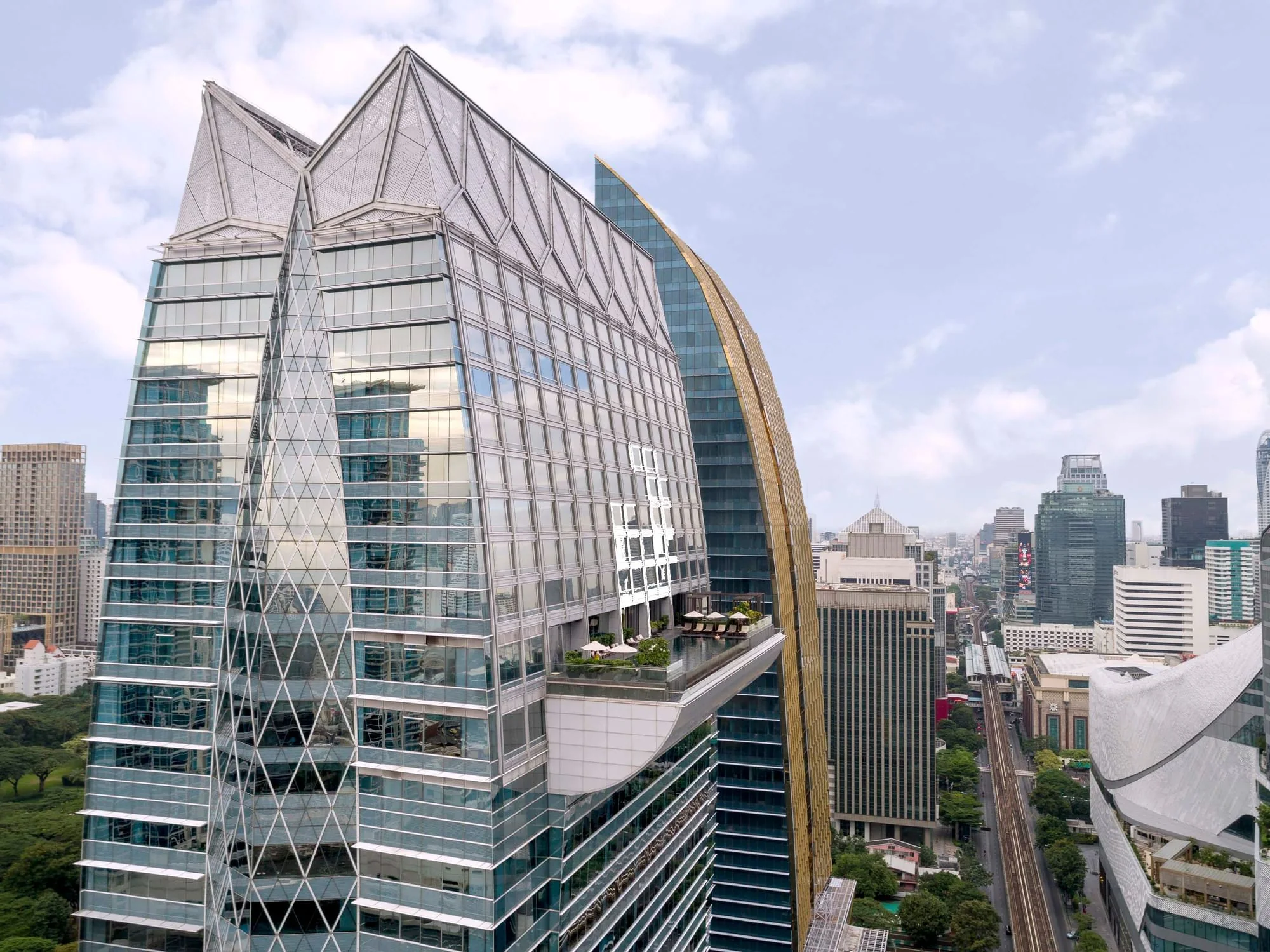 The Okura Prestige Bangkok im gläsernen Turm des Park Ventures Ecoplex mit kantiger silberner Dachkrone und vorspringender Terrasse bei Tageslicht