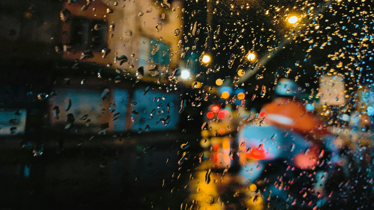 Regentropfen auf einer Scheibe, dahinter Bangkoks Verkehr und Stadtlichter