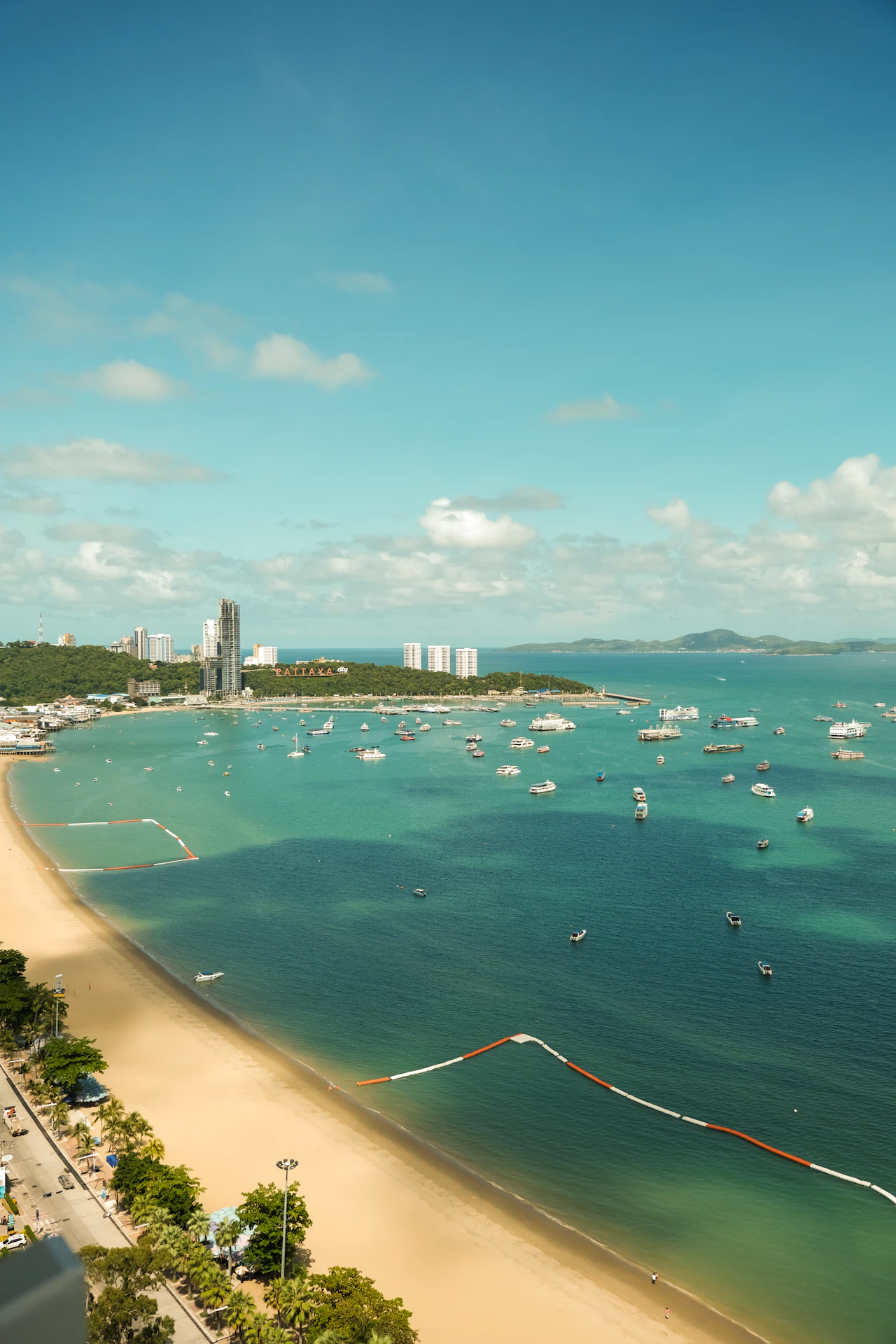 La baia di Pattaya con la spiaggia sabbiosa ad arco, le barche e la scritta Pattaya City sulla collina